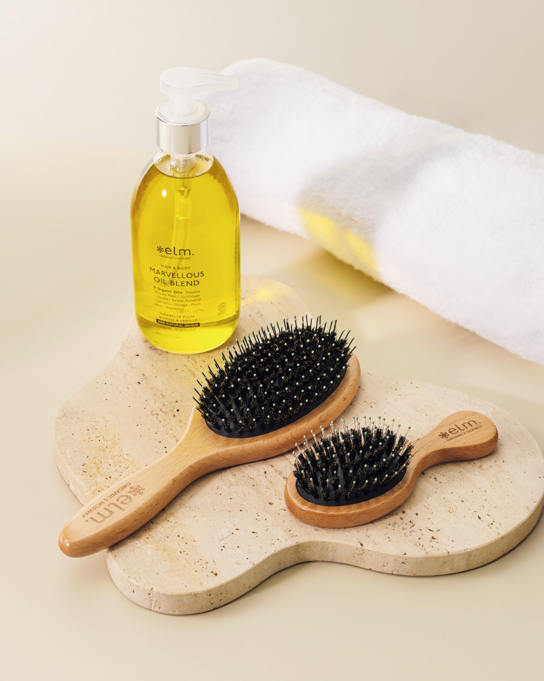 Ease hårbørste i classic og travel size liggende på en beige steinplate med Marvellous Oil blend ved siden av